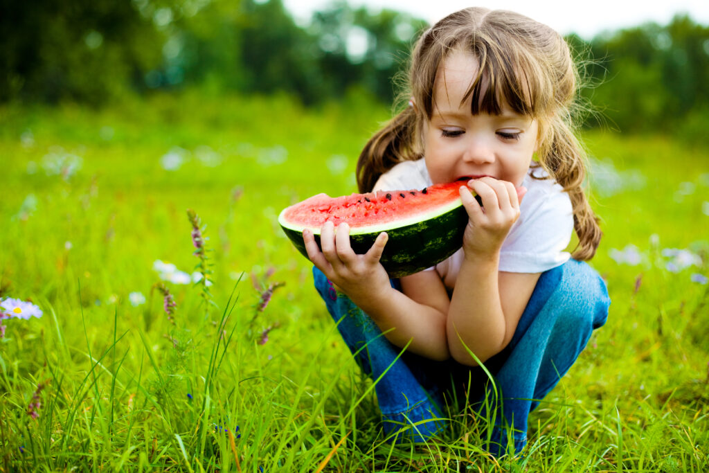 Cute,little,girl,eating,watermelon,on,the,grass,in,summertime